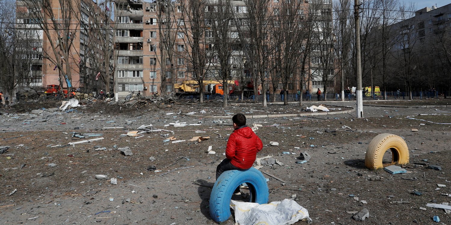 A boy sits in front of a multi-story apartment building destroyed by shelling in occupied Donetsk, March 2022 (Photo: REUTERS/Alexander Ermochenko)