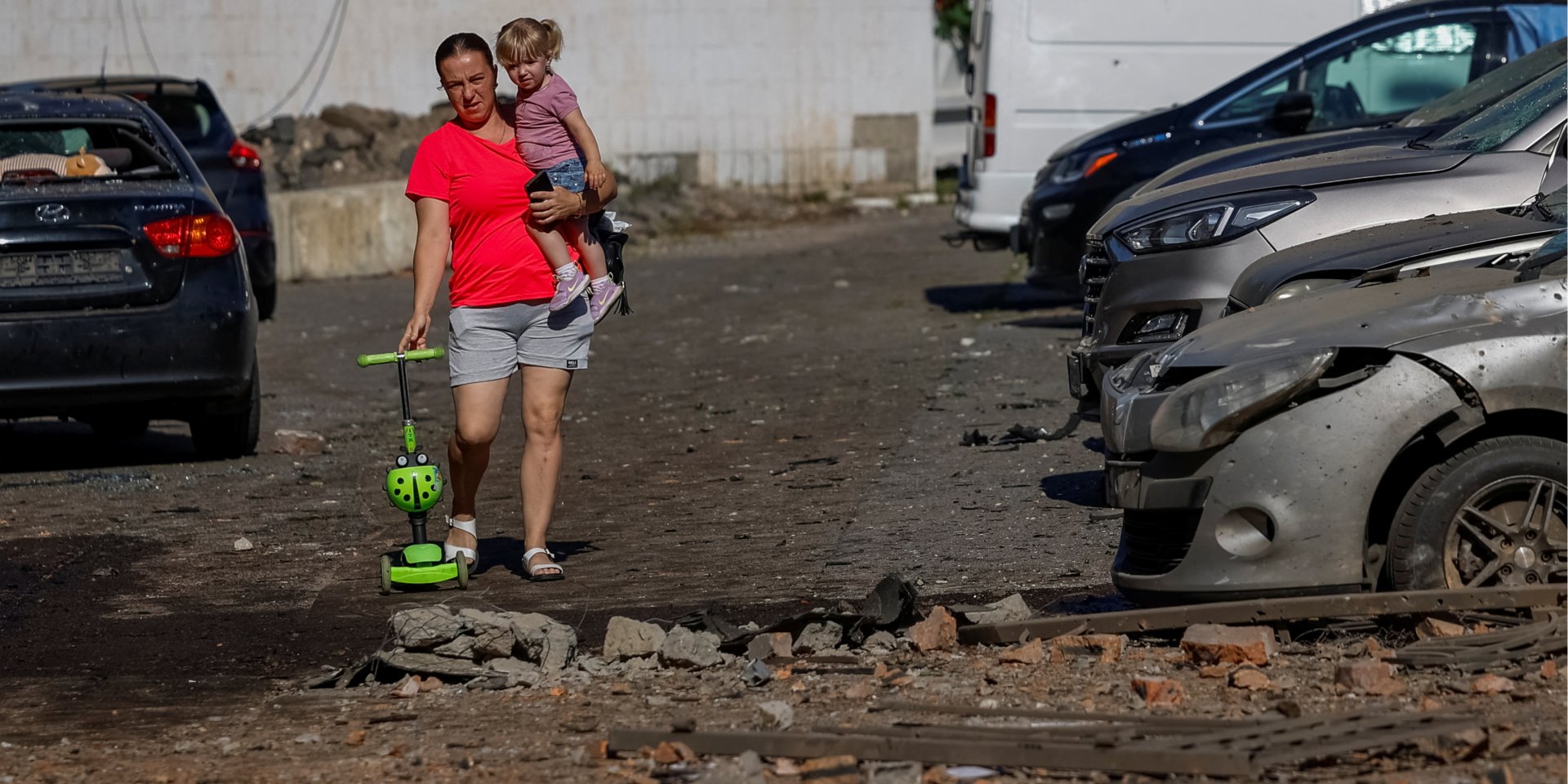 A woman carries her daughter as they pass by damaged vehicles at the site of a school, which was hit during Russian drone and missile strikes, amid Russia's attack on Ukraine, in Kyiv, Ukraine July 4, 2025. (Photo: REUTERS/Alina Smutko)