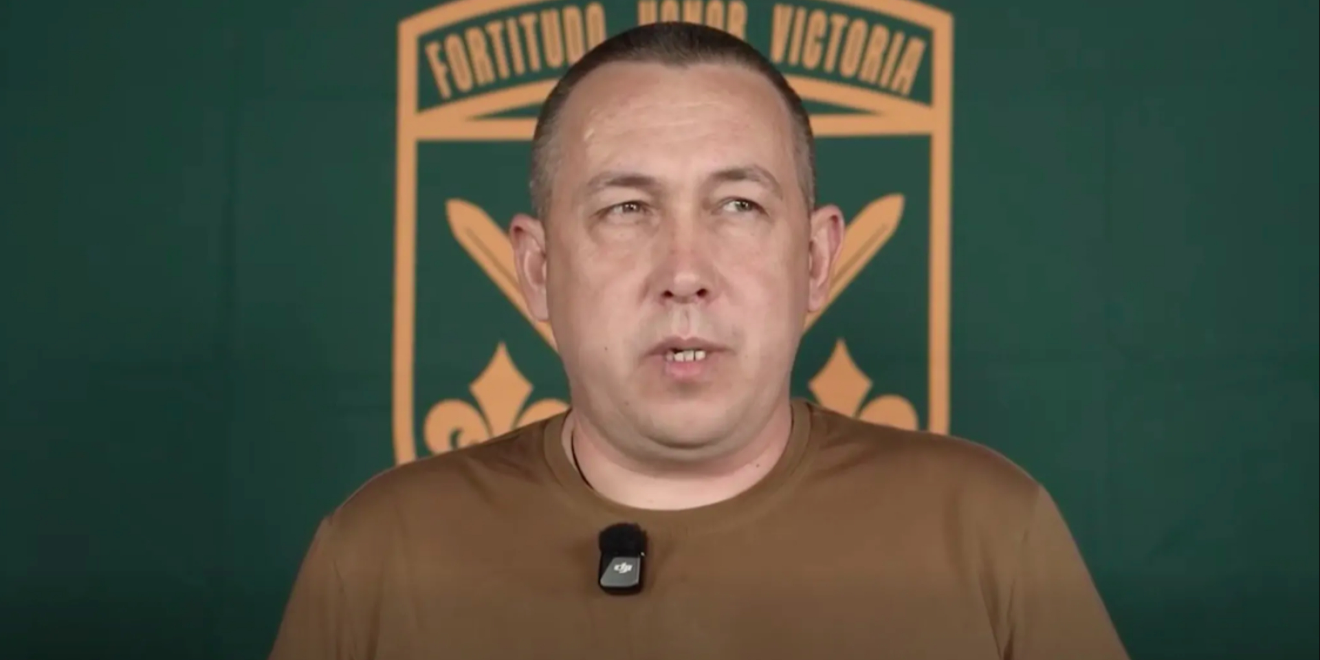 Комбриг Станіслав Лучанов на тлі офіційної емблеми 155 ОМБр з девізом «Fortitudo. Honor. Victoria», що перекладається з латини як «Мужність. Честь. Перемога» (Фото: 155 ОМБр)
